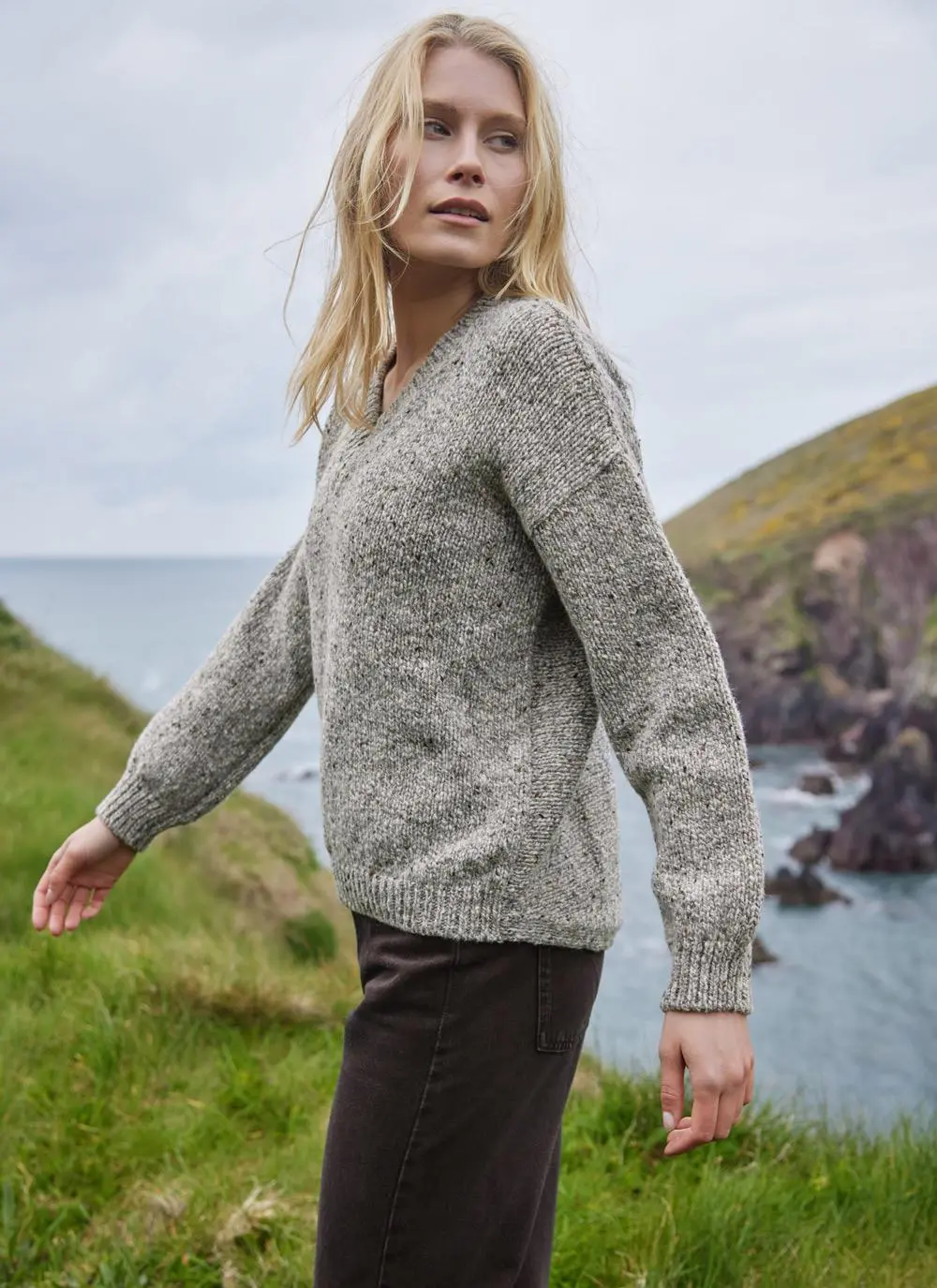 blonde woman standing in front of irish cliffs wearing a grey knit wool sweater
